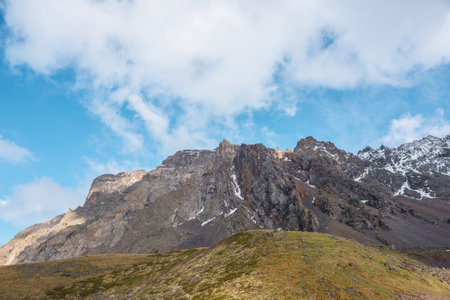 Atmospheric landscape with sharp pinnacle on sunlit high mountain range under clouds in blue sky. Beautiful alpine scenery with peaked mountain top in sunlight under cloudy sky at changeable weather.の写真素材