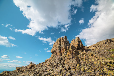 Scenic mountain landscape with stone outliers on rocky hill in sunlight under cloudy sky. Colorful scenery with sunlit sharp rocks on stone mountain under clouds in blue sky at changeable weather.の写真素材