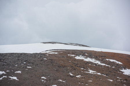 Dramatic landscape with huge rock mountain with snowy mountain dome under gray cloudy sky. Awesome scenery with high snow mountain in dome shape in center at overcast weather. Dome shaped mountain topの写真素材