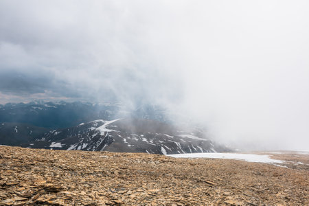 Awesome top view through clouds to high snowy mountains. Scenic landscape with beautiful snow mountains in low clouds. Atmospheric alpine view from stone hill to snow mountain range with low clouds.の写真素材
