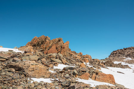Scenic mountain landscape with old rocks and stones among snow in sunlight. Awesome alpine scenery with stone outliers on high mountain under blue sky in sunny day. Sharp rocks at very high altitude.の写真素材