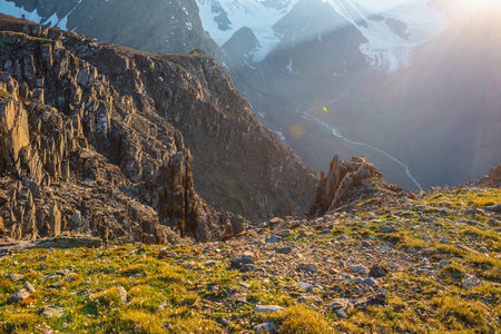 Sunny mountain view from cliff at very high altitude. Scenic alpine landscape with beautiful sharp rocks and couloirs in sunlight. Beautiful scenery on abyss edge with sharp stones and green grass.の写真素材