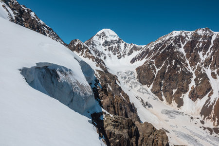 Scenic alpine landscape with snow-covered mountain top and steep glacier tongue with icefall in sunlight. Awesome mountain scenery with pointed peak and glacier on rocks under blue sky in sunny day.の写真素材