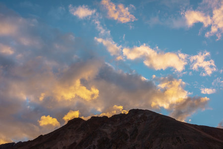 Scenic landscape with dark mountain range silhouette under evening blue sky with vivid orange sunset clouds. Sunlit orange cirrus clouds in sunset sky above mountains silhouettes at changeable weatherの写真素材