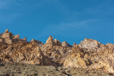 Scenic mountain landscape with sharp rocks under blue sky in sunny day. Colorful scenery with gold sunlit sharp rocky mountains. Sharp rocks in bright sun. High rocky mountains in golden sunlight.の写真素材