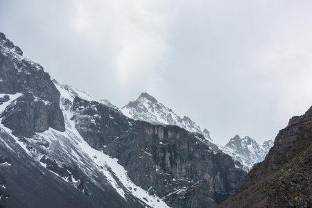 Awesome landscape with high snowy mountain peaked top with sharp rocks in cloudy sky. Dramatic view to snow mountain pointed peak in rainy weather. Atmospheric scenery with white snow on black rocks.の写真素材