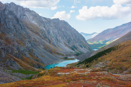 Picturesque landscape with blue alpine lake in colorful autumn valley. Azure mountain lake among multicolor flora. Vivid autumn colors in high mountains. Scenic view from red hill to beautiful lake.の写真素材