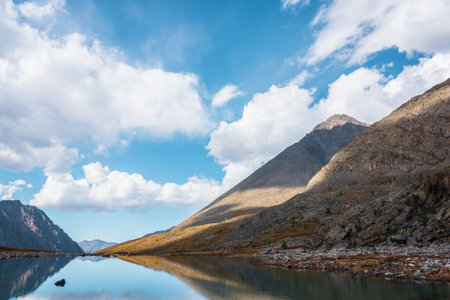 Tranquil autumn landscape with smooth surface of mountain lake in high hanging valley under clouds in blue sky. Meditative view from calm alpine lake to mountain vastness. Glacial lake clear water.の写真素材