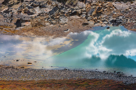 Abstract nature background with sunlight through clouds reflected in turquoise mountain lake mirror. Beautiful pure alpine lake with cloudy sky reflection among vivid autumn colors in high mountains.の写真素材