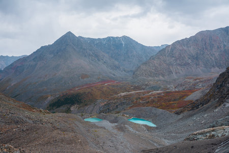 Awesome aerial view to turquoise eyes-lakes and pyramid shaped high mountain under dramatic gray cloudy sky. Two beautiful mountain lakes among fading autumn colors in overcast. Small glacial lakes.の写真素材