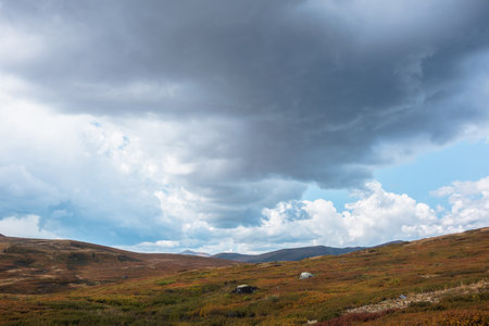 Beautiful autumn landscape of high mountain plateau under dramatic cloudy sky. Fading autumn colors in mountains in overcast. Atmospheric mountain scenery of tableland under clouds in rainy weather.の写真素材