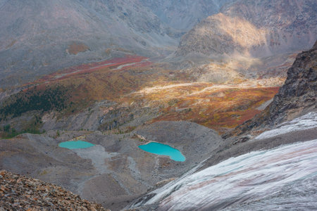 Awesome aerial view to turquoise eyes-lakes in mountain valley. Two beautiful small mountain lakes among fading autumn colors in bright sun. Scenic top view to glacial lakes among multicolor mountainsの写真素材