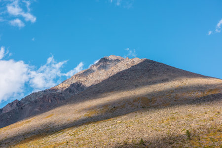 Colorful landscape with pyramid shaped mountain top in center of blue sky. Large pointy peak in sunlight with shadows of clouds. Sharp rocks on high pinnacle in sunny day. Big mountain in pyramid formの写真素材