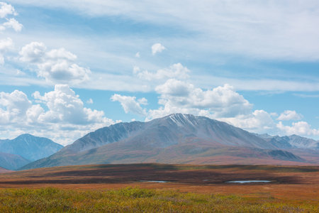 Motley autumn landscape with sunlit high mountain plateau with lakes and beautiful mountain top under dramatic cloudy sky. Vivid autumn colors in mountains. Shadows of clouds in changeable weather.の写真素材