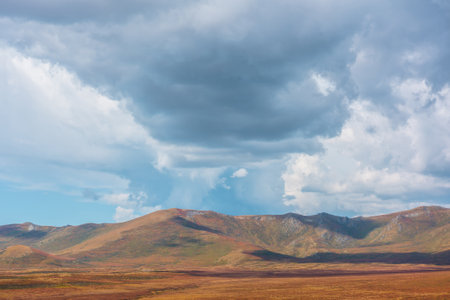 Motley autumn landscape with sunlit high mountain plateau and mountain range under dramatic sky. Vivid autumn colors in mountains. Sunlight and shadows of clouds in changeable weather. Sunny and rainyの写真素材