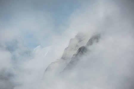 Lovely scenery with big snowy mountains in thick clouds. High mountain wall in gantly cloudy sky. Scenic view to large snow mountain in clearance of dense fog. Beautiful diagonal rocks in low clouds.の写真素材