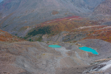 Awesome aerial view to turquoise eyes-lakes in mountain valley. Two beautiful small mountain lakes among fading autumn colors in overcast. Scenic top view to glacial lakes among multicolor mountains.の写真素材