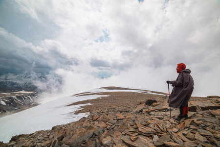 Awesome minimalist mountain landscape with hiker at very high altitude in dense low clouds. Wonderful alpine scenery with man on stone hill with snow in thick clouds. Man and majestic mountains natureの写真素材
