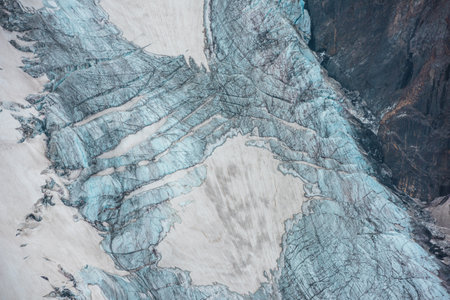 Beautiful mountain landscape with vertical glacier tongue with cracks among rocks. Awesome natural backdrop of large glacier with icefall. Nature texture of mountain glacier with fissures close up.の写真素材