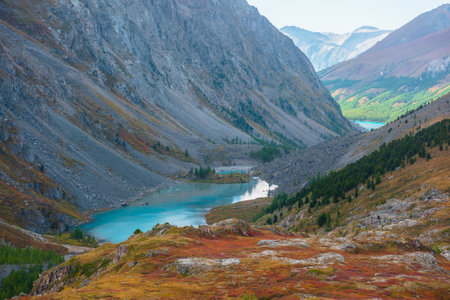 Picturesque landscape with blue alpine lake in colorful autumn valley. Azure mountain lake among multicolor flora. Vivid autumn colors in high mountains. Scenic view from red hill to beautiful lake.の写真素材