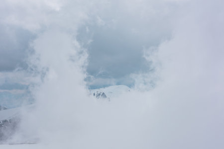 Awesome aerial view to high snowy mountain in dense low clouds. Minimal landscape with beautiful mountain peak in thick clouds. Simple minimalism with snow mountain top in cloudy sky above low clouds.の写真素材