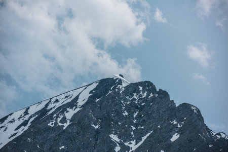 Beautiful landscape with high mountain pointy peak with snow cornice in clouds in blue sky. Atmospheric mountain scenery with large pinnacle in cloudy sky. Scenic evening view to peaked mountain top.の写真素材