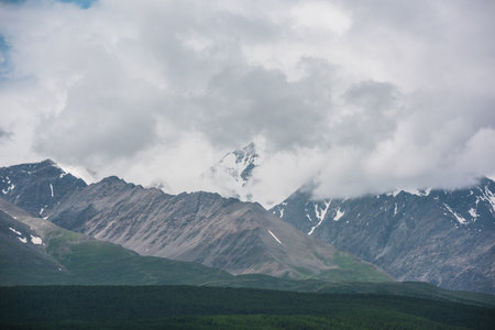 Dramatic aerial view to large snow mountain range under rainy cloudy sky. Dark atmospheric alpine scenery with high snowy mountain peak in low clouds. Gloomy landscape with mountain top in overcast.の写真素材