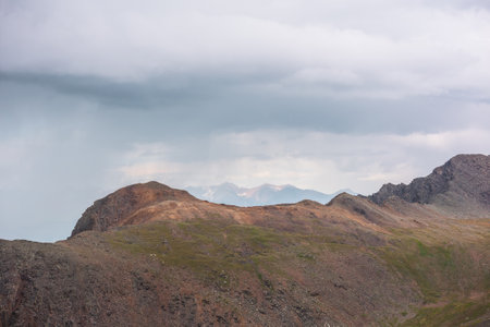 Dramatic aerial landscape with sunlit mountain top during rain at changeable weather. Atmospheric mountain scenery with sharp rocks in sunlight under lead gray cloudy sky. Rainy clouds in mountains.の写真素材