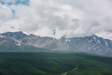 Dramatic aerial view to large snow mountain range under rainy cloudy sky. Dark atmospheric alpine scenery with high snowy mountain peak in low clouds. Gloomy landscape with mountain top in overcast.の写真素材