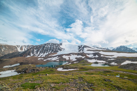 Colorful green landscape with turquoise mountain lake among sunlit rocks and snow mountains under cloudy sky in changeable weather. Awesome sunny scenery with two glacial lakes and snow mountain top.の写真素材