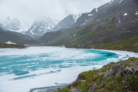 Atmospheric mountain landscape with frozen alpine lake during snowfall. Awesome cold scenery with snowfall in high mountain valley with icy mountain lake on background of snow mountains in low clouds.の写真素材