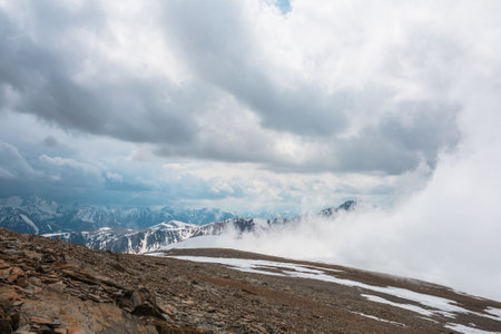 Awesome top view to high snowy mountain in dense low clouds. Scenic mountain landscape with beautiful peaks in thick clouds. Atmospheric view from stone hill to snow mountain tops among low clouds.の写真素材