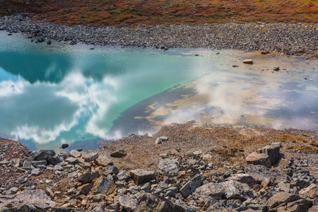 Abstract nature background with sunlight through clouds reflected in turquoise mountain lake mirror. Beautiful pure alpine lake with cloudy sky reflection among vivid autumn colors in high mountains.の写真素材