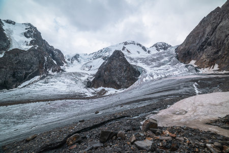 Dramatic landscape with two glacier icefalls on large snow mountain range with sharp rocks under gray cloudy sky. Long glacier with icefall in high altitude. Gloomy scenery in mountains in overcast.の写真素材