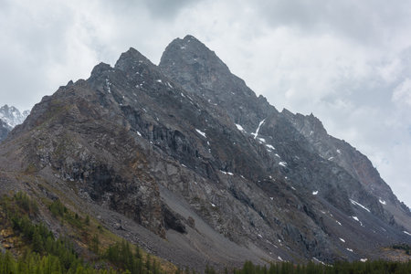 Atmospheric mountain landscape with large pointy pinnacle under gray cloudy sky. Gloomy scenery with high pointed mountain peak with sharp rocks in low clouds. Huge rocky peaked top in rainy weather.の写真素材