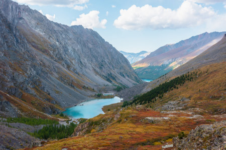 Picturesque landscape with blue alpine lake in colorful autumn valley. Azure mountain lake among multicolor flora. Vivid autumn colors in high mountains. Scenic view from red hill to beautiful lake.の写真素材