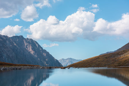 Tranquil autumn landscape with smooth surface of mountain lake in high hanging valley under clouds in blue sky. Meditative view from calm alpine lake to mountain vastness. Glacial lake clear water.の写真素材