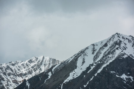 Awesome landscape with high snowy mountain range with sharp rocks in sunlight in cloudy sky. Dramatic view to snow mountains in changeable weather. Atmospheric scenery with white snow on black rocks.の写真素材