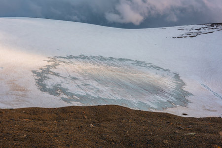 Dramatic landscape with glacier on sunlit high snow mountain under cloudy sky at sunset. Beautiful alpine landscape with large snowy mountain in sunlight under evening clouds at changeable weather.の写真素材