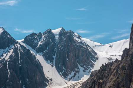 Scenic alpine landscape with snowy mountain peak in sunny day. Awesome landscape with rocky pinnacle with snow in sunlight. Beautiful view to snow mountain top and sharp rocks at very high altitude.の写真素材
