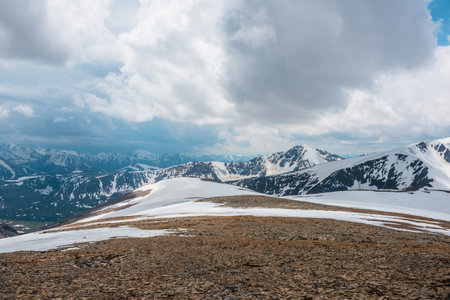Awesome alpine scenery with snow mountains under cloudy sky. Scenic mountain landscape at very high altitude in overcast. Beautiful atmospheric view from stone hill with snow to snowy mountain range.の写真素材