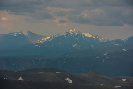 Awesome aerial view to high snow mountain peak in sunlight in overcast. Atmospheric mountain landscape at high altitude with cloudiness. Alpine view to snowy mountain top in light under cloudy sky.の写真素材