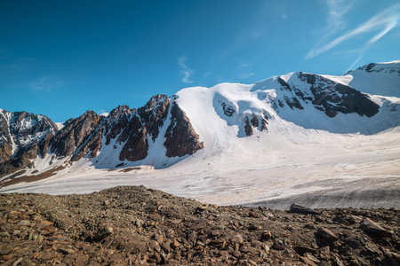 Scenic mountain landscape with large glacier in sunlight. Awesome snowy scenery with glacial tongue under cirrus clouds. Beautiful alpine view to snow mountain tops at very high altitude in sunny day.の写真素材