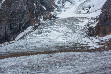 Beautiful glacier with icefall among rocks close-up. Nature background with large glacier tongue. Natural texture of big icefall. Atmospheric mountain landscape in high altitude. Stones on glacial iceの写真素材