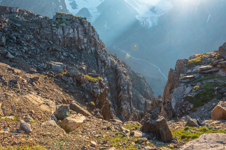 Sunny mountain view from cliff at very high altitude. Scenic alpine landscape with beautiful sharp rocks and couloirs and large glacier in sunlight. Beautiful scenery on abyss edge with sharp stones.の写真素材