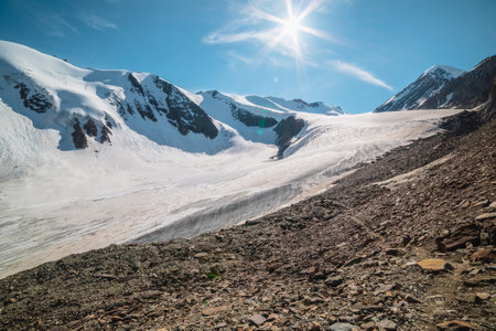 Scenic mountain landscape with large glacier in sunlight. Awesome scenery with glacial tongue under sun in blue sky. Beautiful alpine view to snow mountain tops at very high altitude in sunny day.の写真素材