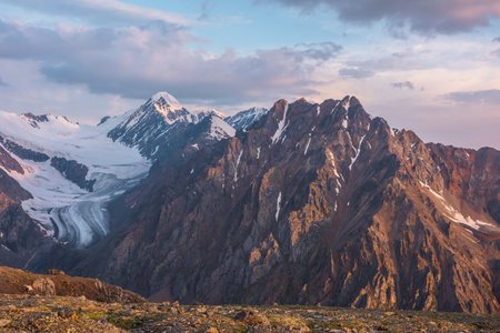 Vivid alpine landscape with high snow mountains and large glacier in sunrise colors. Colorful mountain scenery with sunlit golden rocks and mountains at sunrise. Early morning at very high altitude.の写真素材