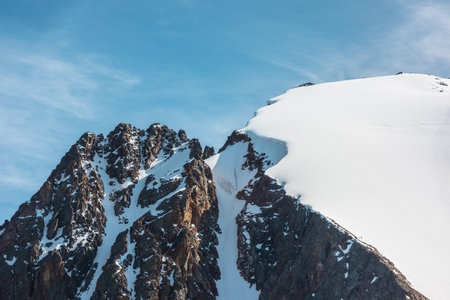 Minimalist alpine landscape with snow-covered mountain top and sharp rocks in sunlight. Simple minimalism with snowbound mountain in blue sky. Minimal view to snow mountain peak at very high altitude.の写真素材