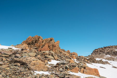 Scenic mountain landscape with old rocks and stones among snow in sunlight. Awesome alpine scenery with stone outliers on high mountain under blue sky in sunny day. Sharp rocks at very high altitude.の写真素材