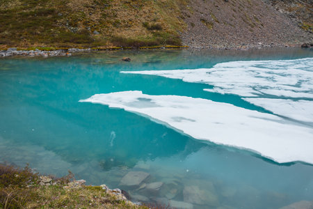 Beautiful mountain landscape with frozen alpine lake and stones in transparent water. Clear ice floats on water surface of mountain lake. Awesome scenery with icy mountain lake. Ice lake background.の写真素材
